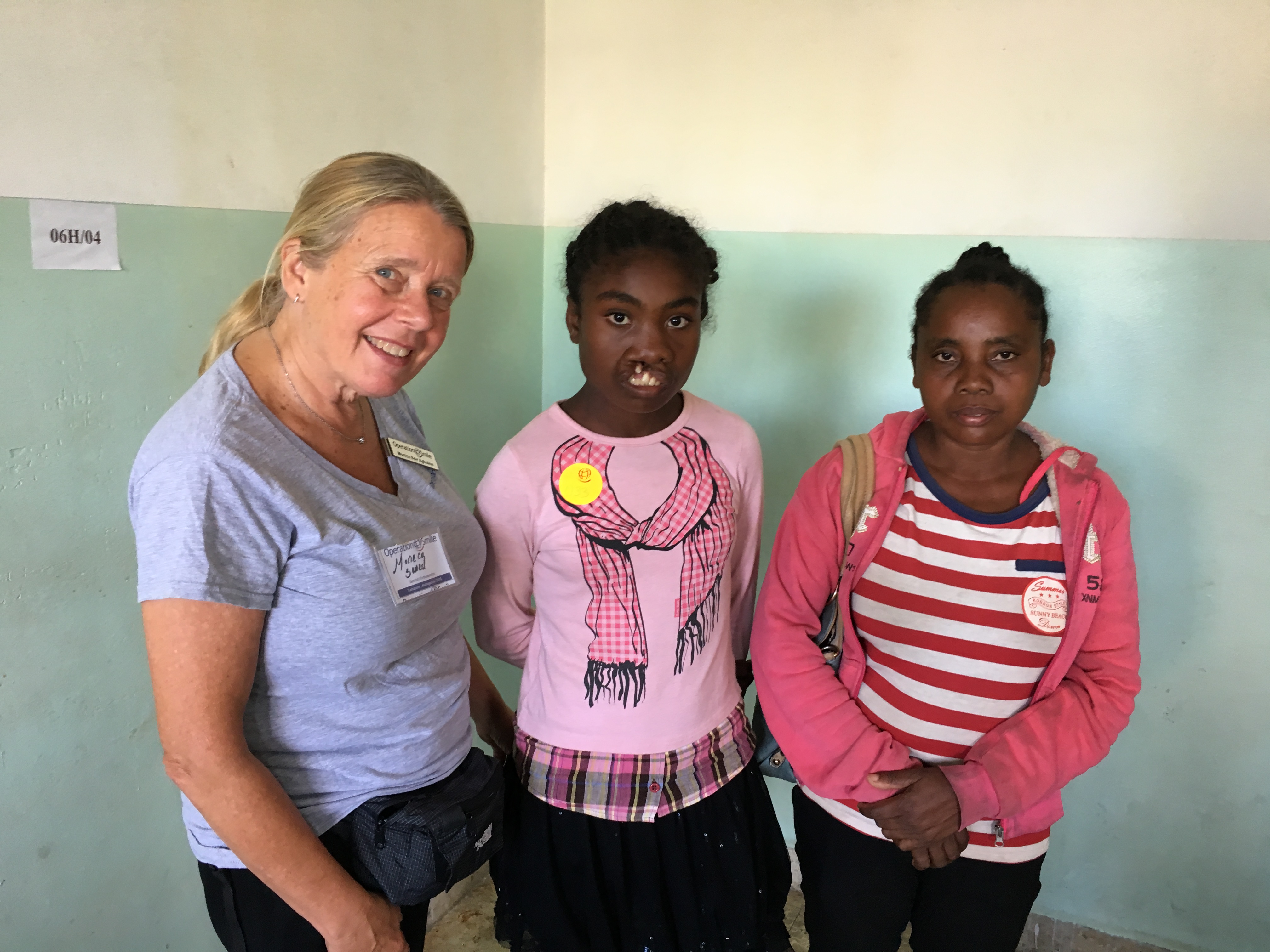 Tandläkaren Monica står tillsammans med en tonårig tjej med läpp-käk-gomspalt och anhörig. Monica bär en namnbricka och flickan har ett klistermärke med Operation Smiles logotyp på bröstet.