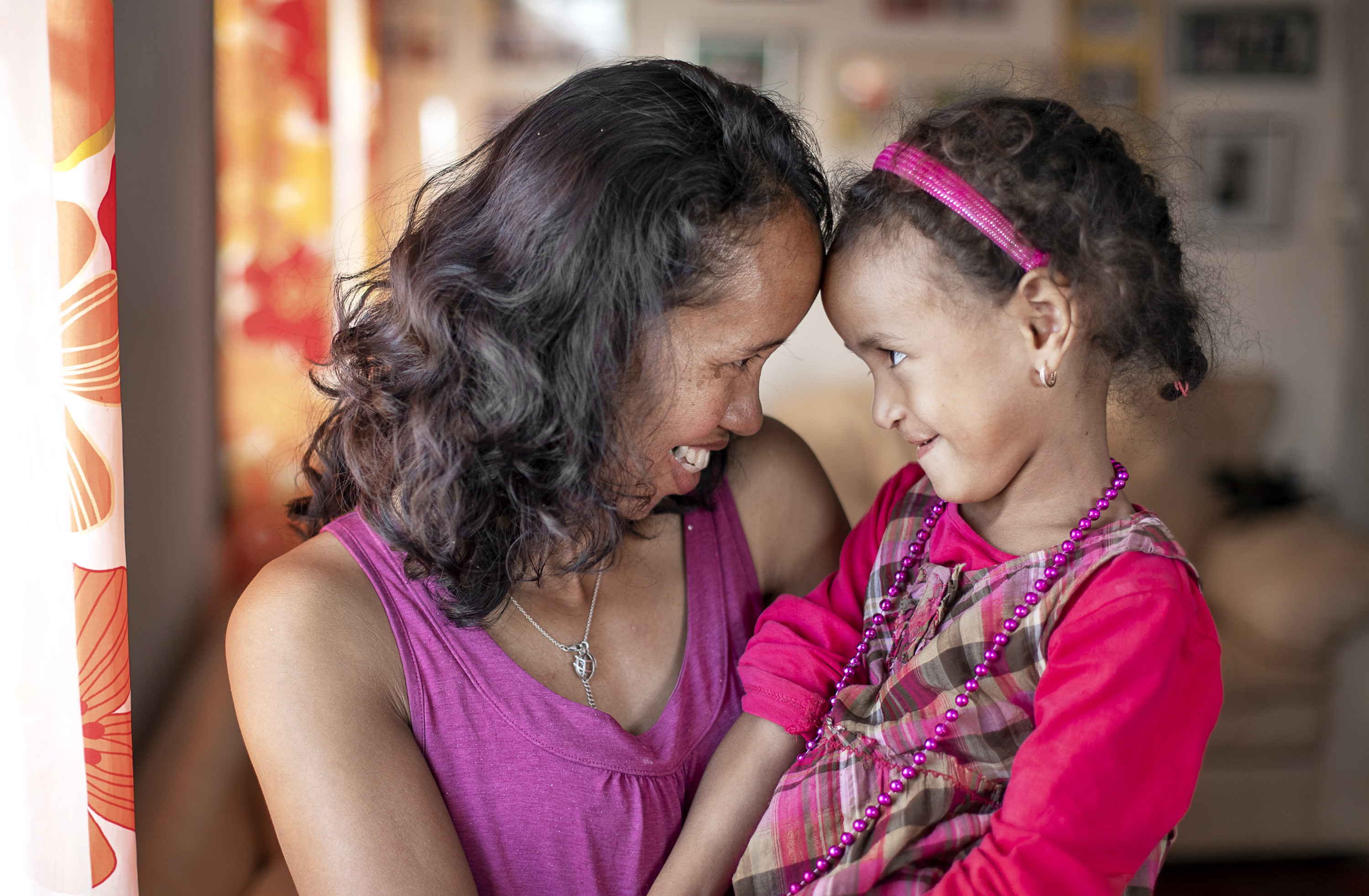 En kvinna och en liten flicka, hennes dotter, syns i profil. Panna mot panna ser de på varandra och ler.