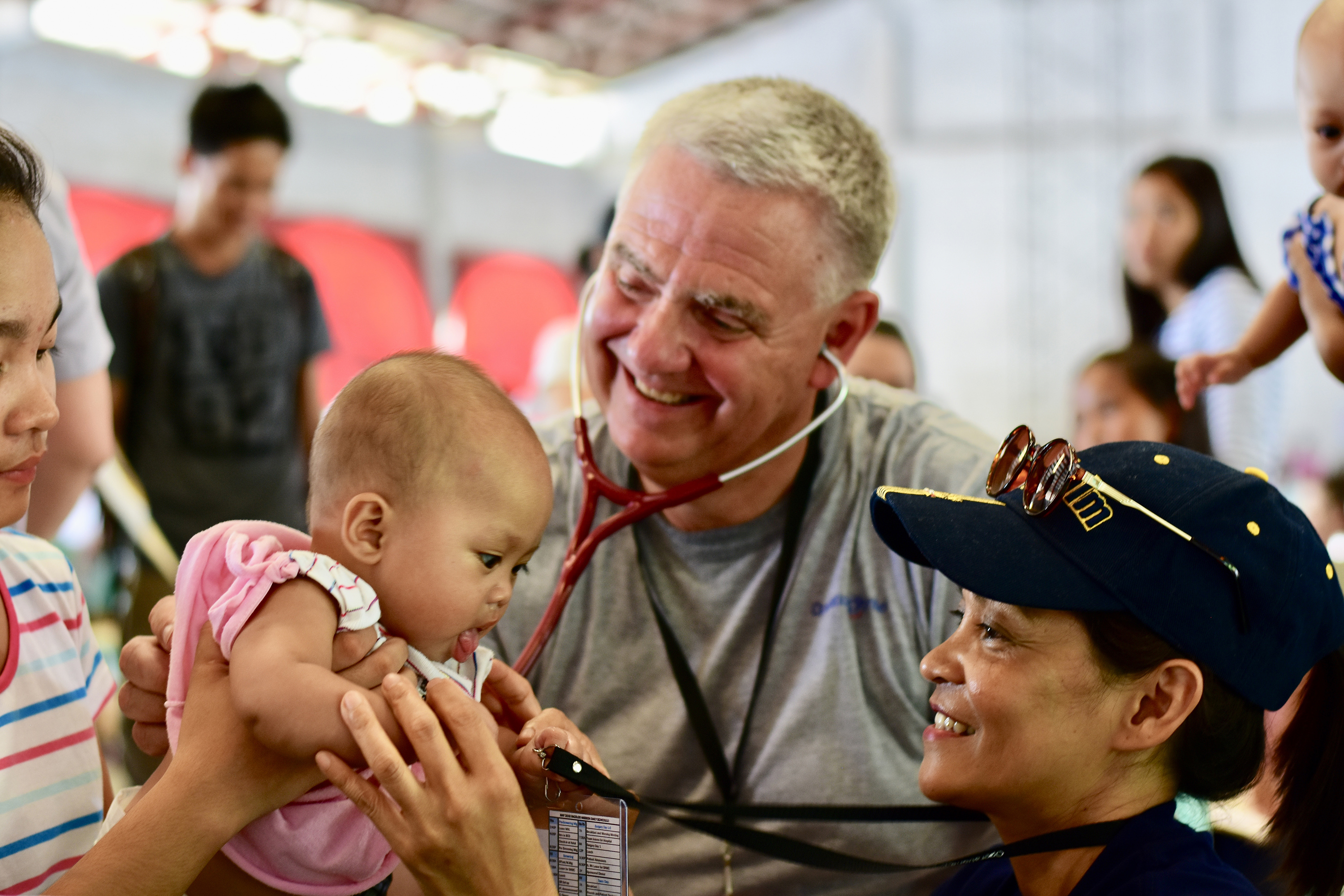 Ett spädbarn blir undersökt med stetoskop som en man håller i. En volontärsköterska leker samtidigt med det lilla barnet.