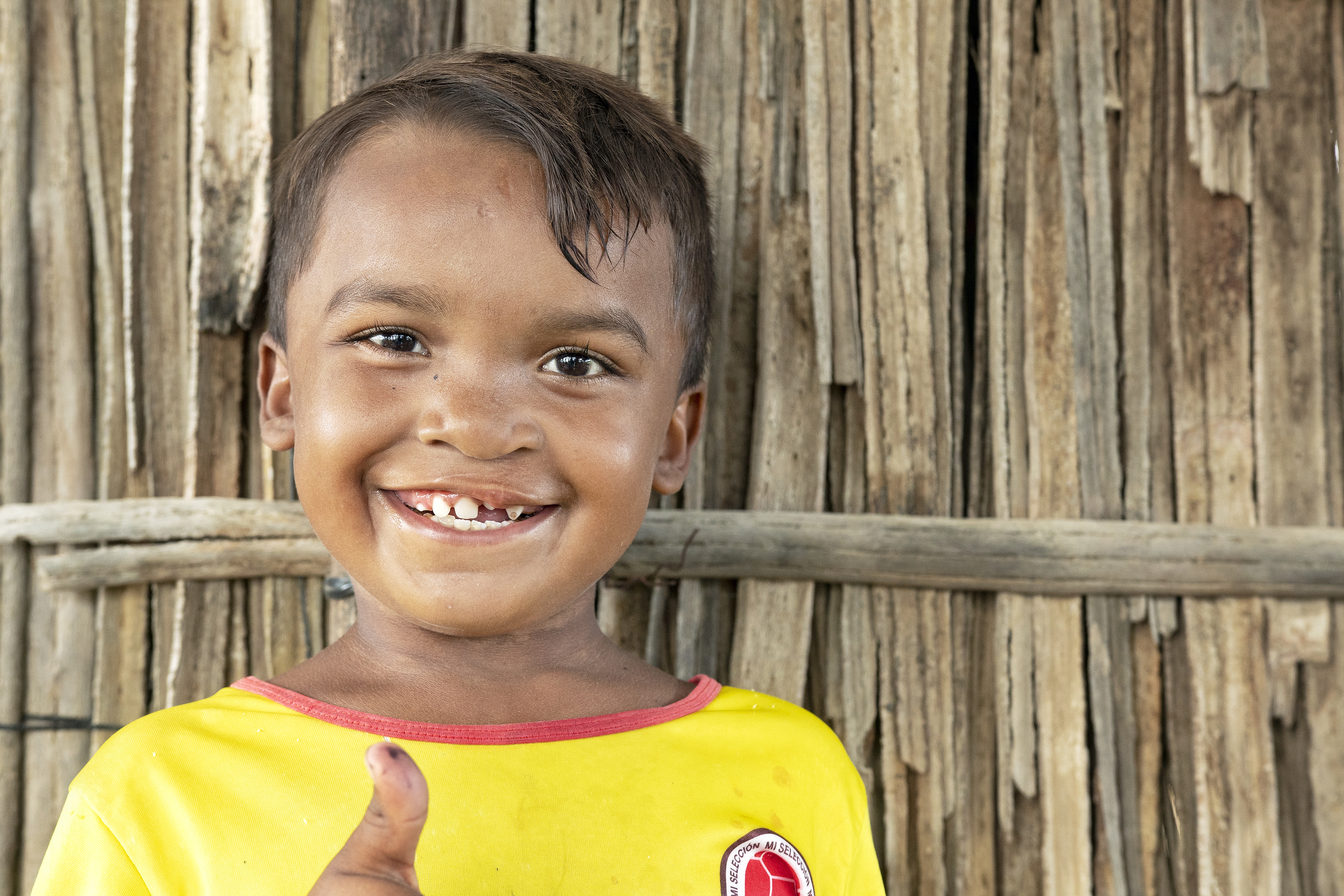 En pojke i gul t-shirt ser rakt mot kameran och ler stort. Han gör tummen upp.