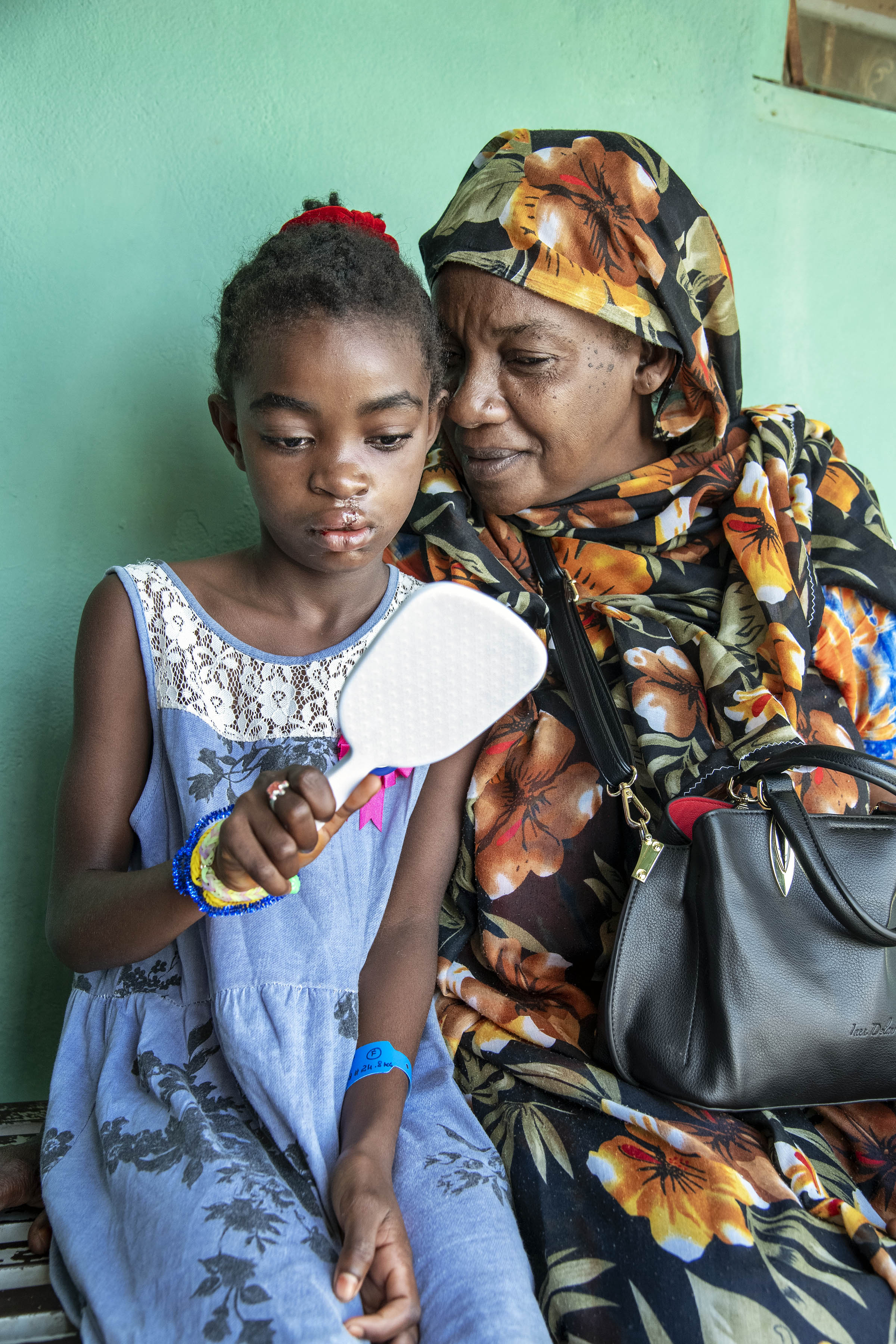 En äldre kvinna och en 10-årig flicka sitter bredvid varandra. Flickan håller i en spegel och betraktar sitt ansikte.