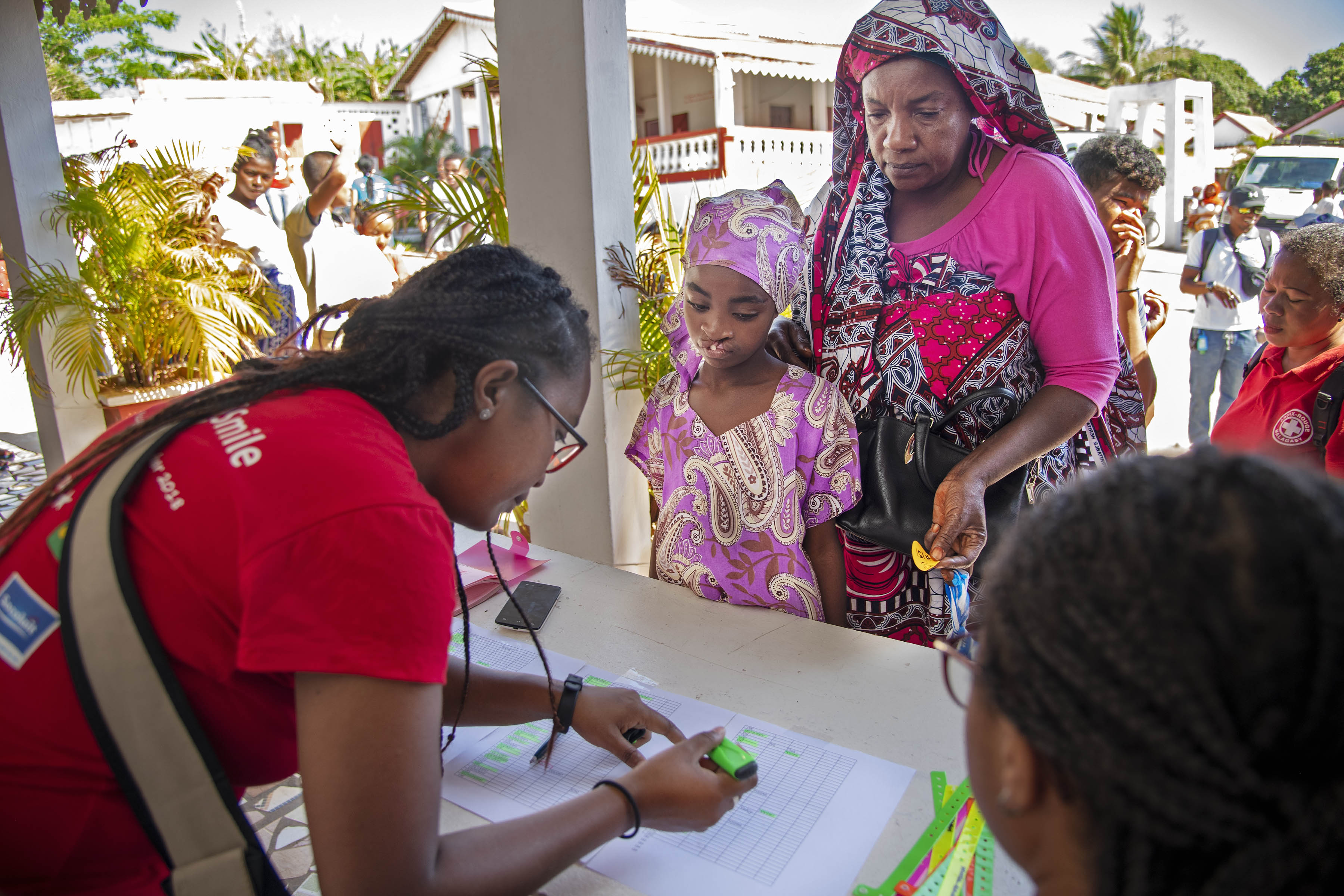 En flicka och en ädre dam står framför ett bord där en annan kvinna gör markeringar i några papper.