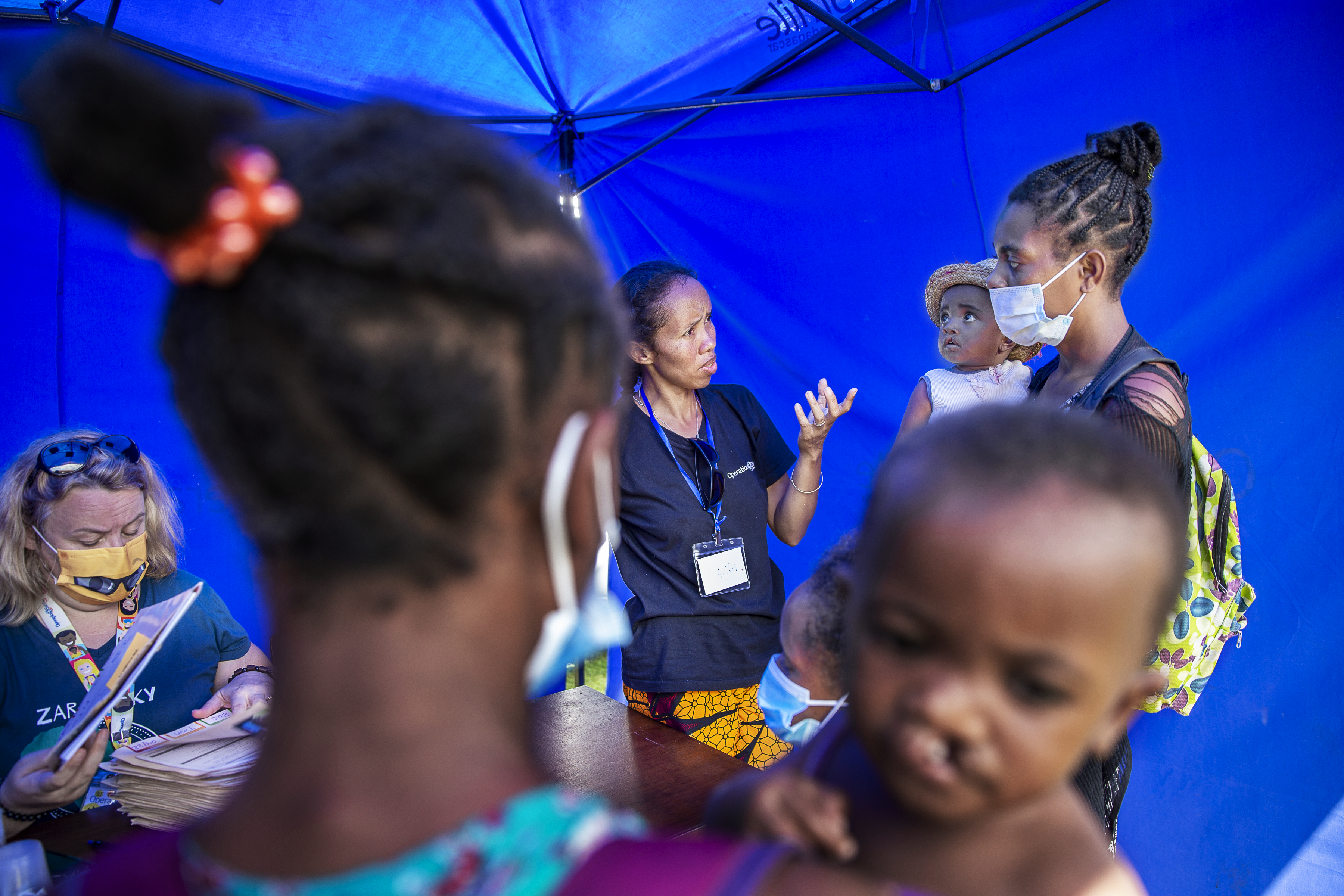 Nina står i ett tält och pratar med en mamma som bär på sitt barn med läppspalt. I förgrunden syns en annan mamma som också bär på sitt barn med läpp-käk-gomspalt.