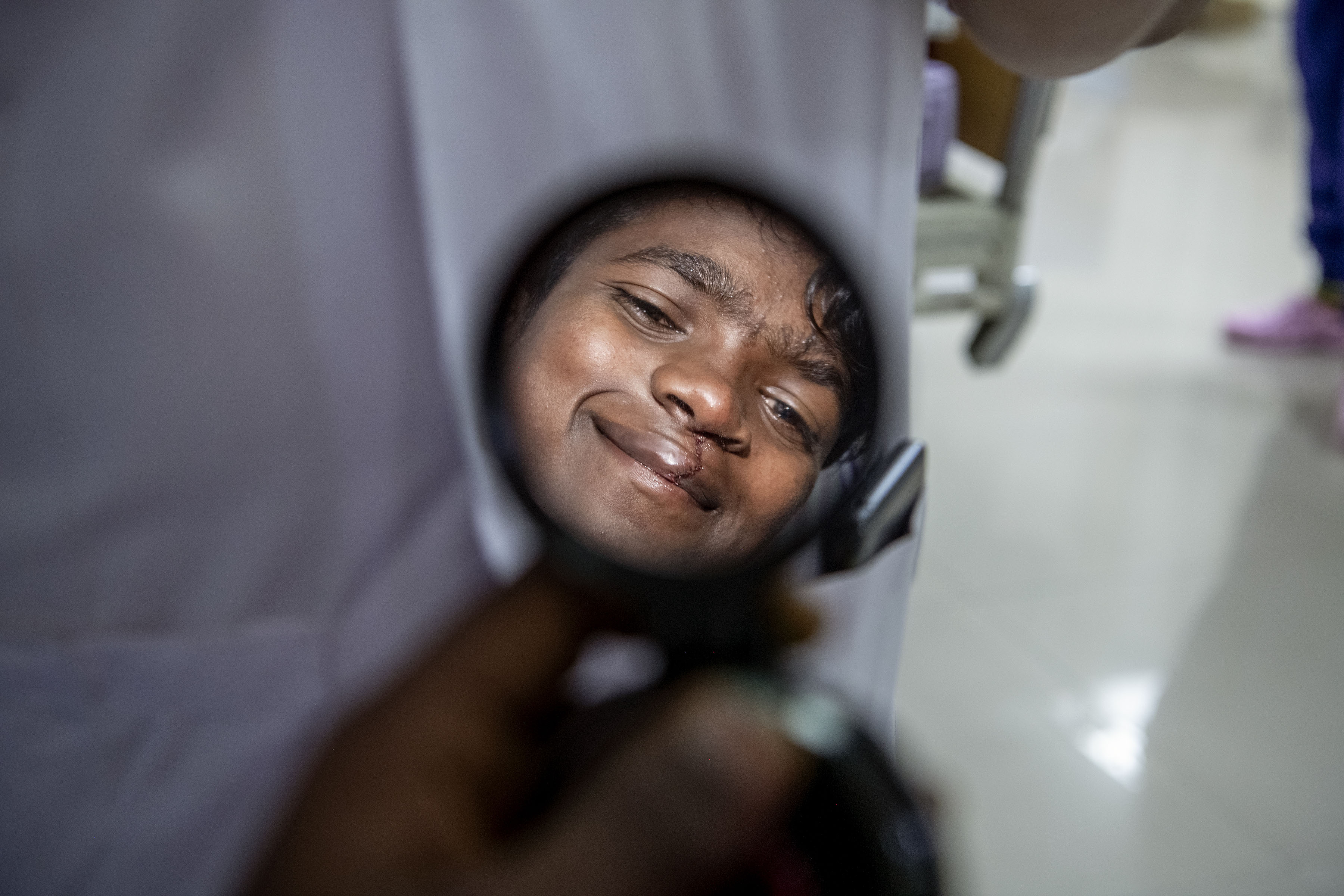 En persons ansikte speglas i en rund handhållen spegel som hålls nära hakan, med en suddig bakgrund.