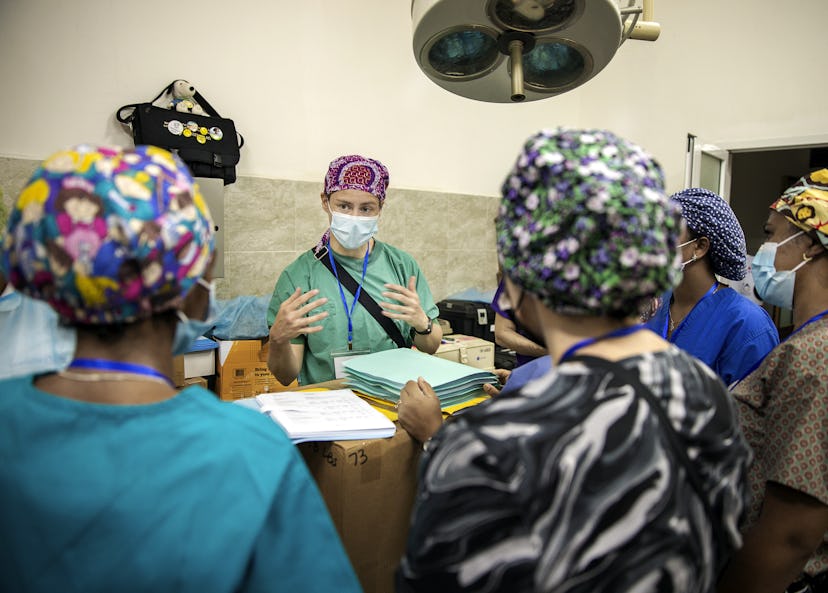 En vårdpersonal i operationskläder och munskydd pratar med kollegor i samma klädsel i ett sjukhusrum under operationslampa.