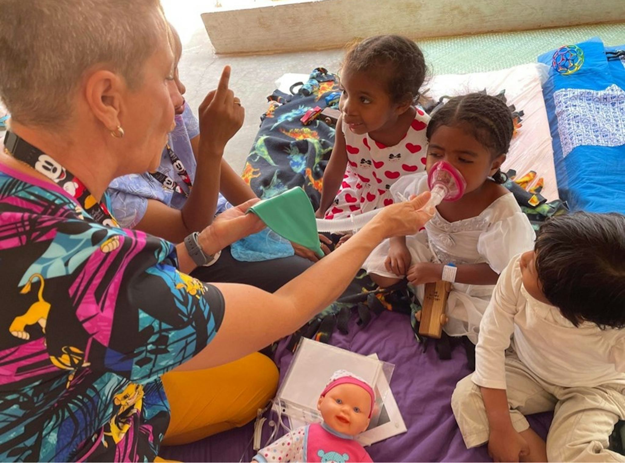 En kvinna visar några barn hur en narkosmask fungerar för att göra dem trygga inför sin operation.