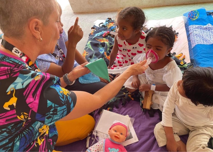 En kvinna visar några barn hur en narkosmask fungerar för att göra dem trygga inför sin operation.