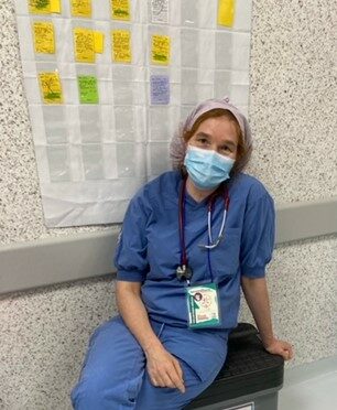 Volontären Helena är iklädd operationskläder och ansiktsmask. Hon sitter i en sjukhuskorridor och tittar in i kameran. Hon har stetoskop och namnbricka runt halsen.