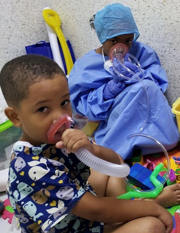 Vårdpersonal visar ett barn hur man andas i en mask som förberedelse inför sövning.