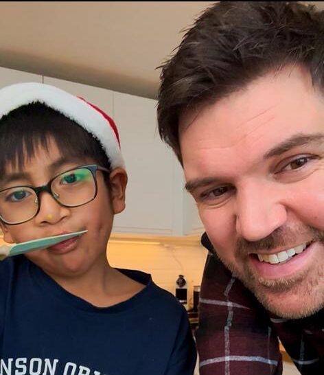 Ett barn med tomteluva borstar tänderna bredvid en vuxen man i ett kök.