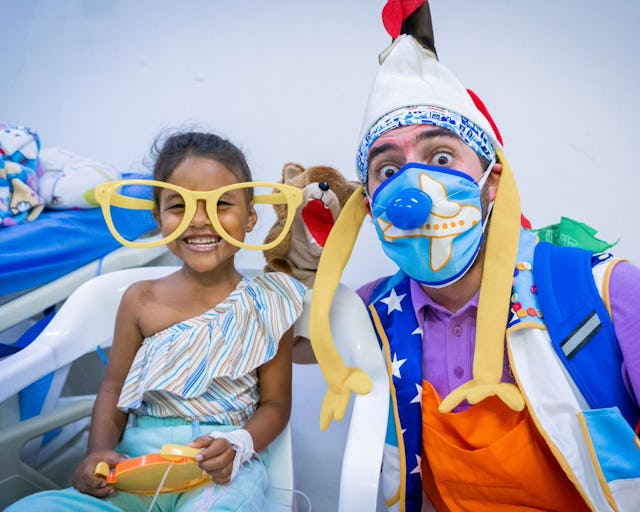 Flicka med stora leksaksglasögon tillsammans med en clown i sjukhusmiljö