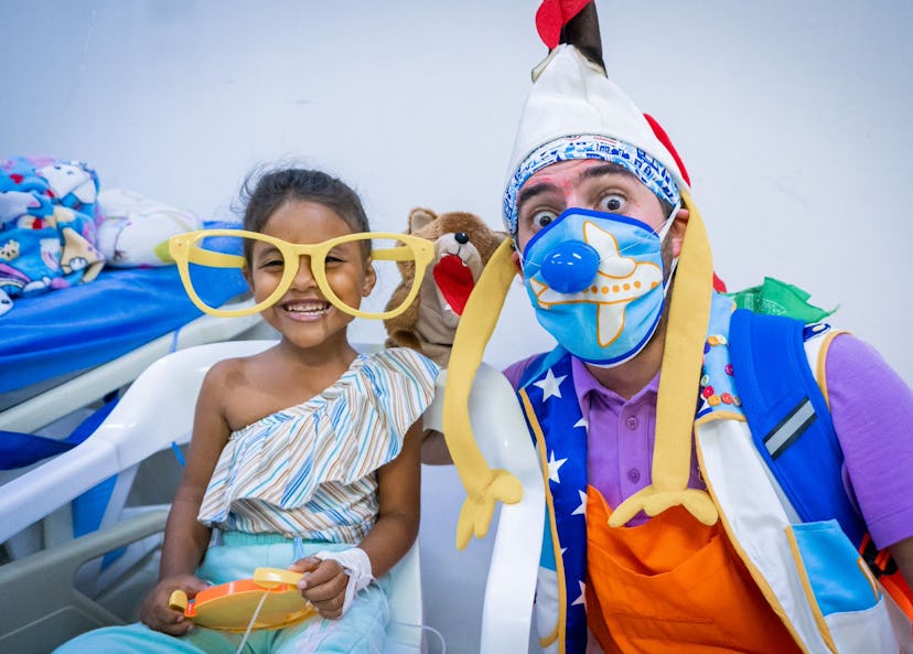 Flicka med stora leksaksglasögon tillsammans med en clown i sjukhusmiljö