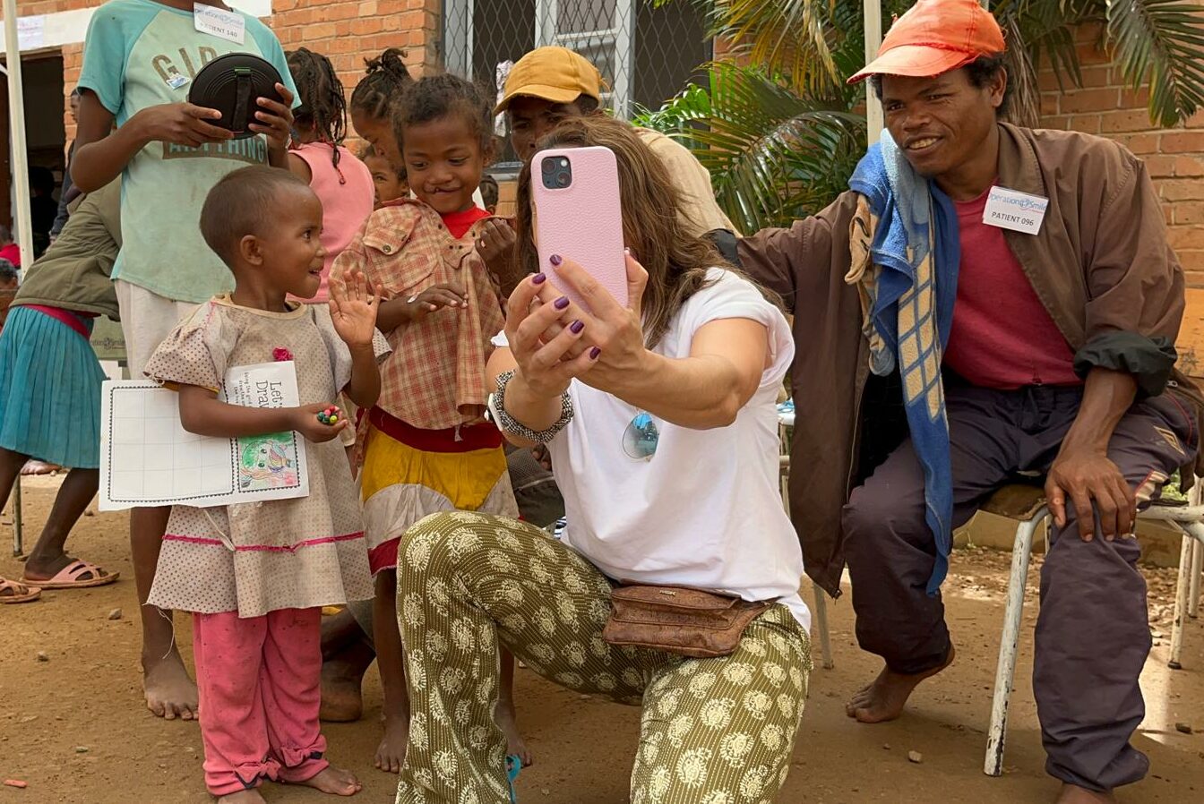 Reporter sitter på huk och tar en bild med sin mobiltelefon tillsammans med några barn.