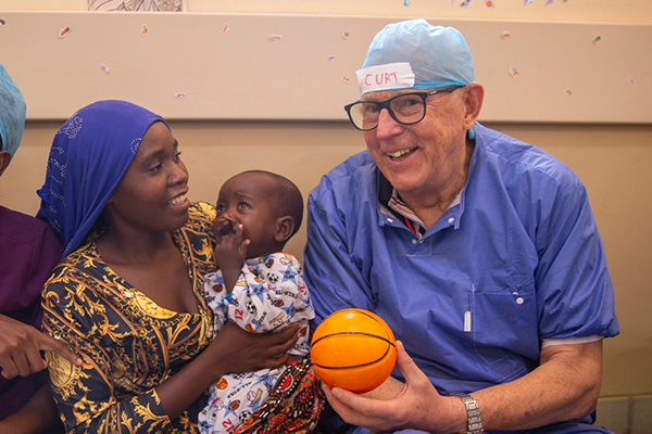 Curt sitter med en mamma och ett barn. Curt håller i en liten basketboll och ler in i kameran.