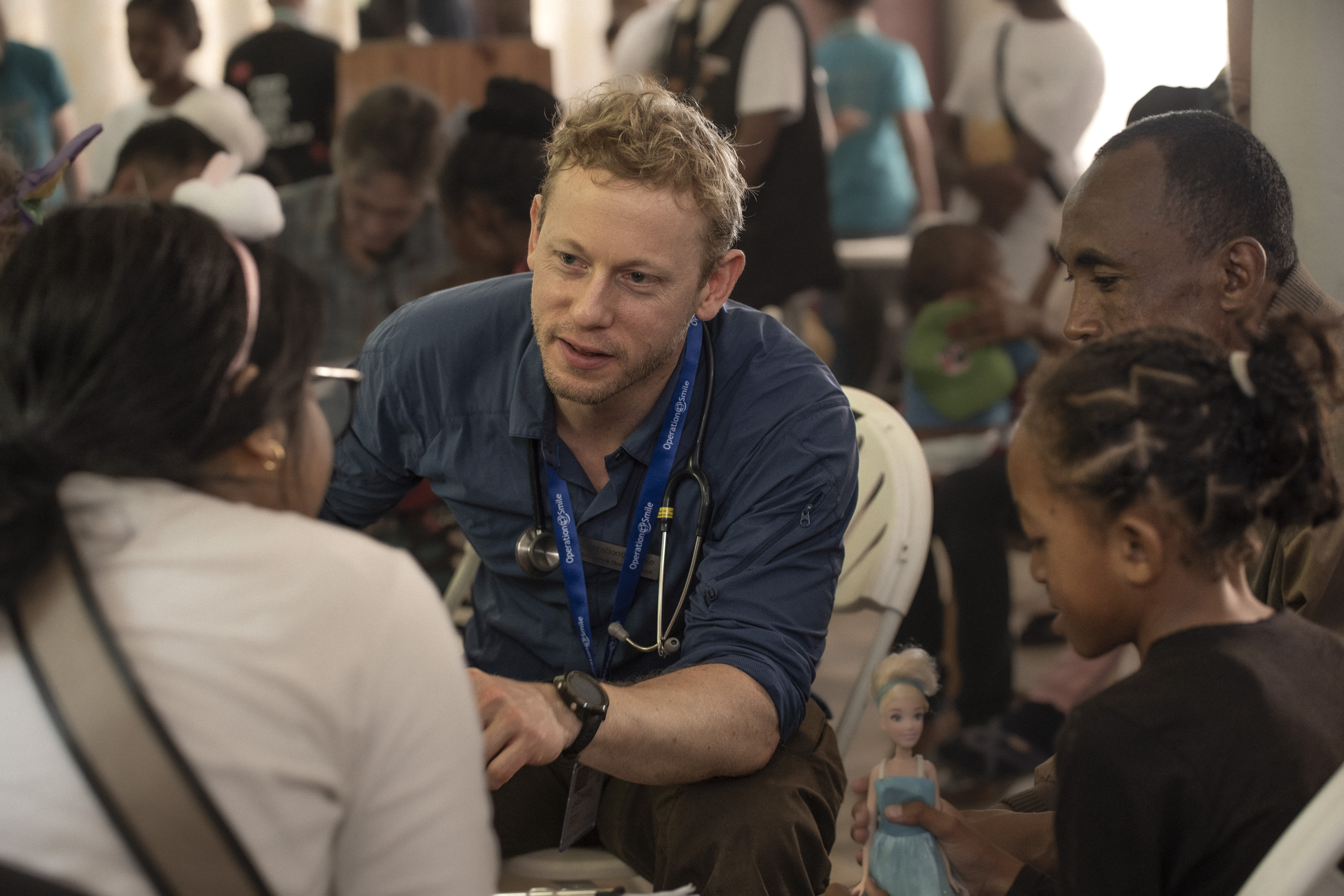 Volontären Johannes pratar med en kvinna. Han sitter framåtlutad och har ett stetoskop runt halsen.