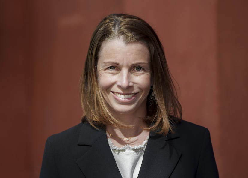 Närbild på en leende Malin Söderström framför en rödfärgad bakgrund. Hon har axellångt brunt hår och är klädd i mörk kavaj och en vit blus.