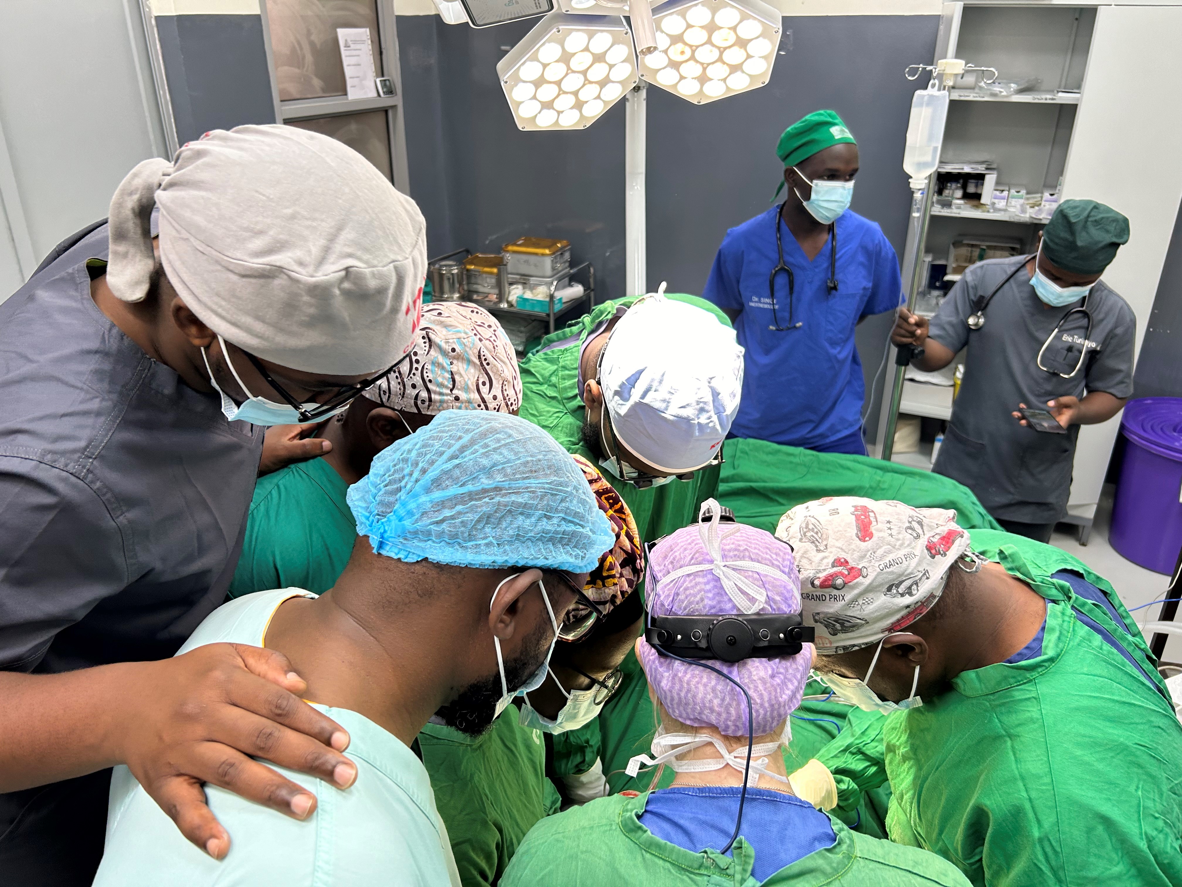 Flera personer i operationskläder ser på medan en kirurg och en assistent opererar. Kirurgen sitter med ryggen mot kameran.