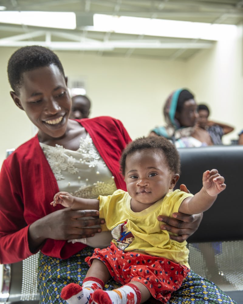 En bebis sitter i knät på en kvinna. De befinner sig i ett väntrum och fler personer skymtar i bakgrunden.