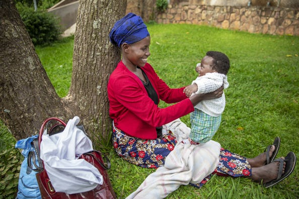 Mamma och son före operationen, sitter på gräset lutade mot ett träd. Hon leker med honom och båda ser mycket glada ut när de tittar på varandra.