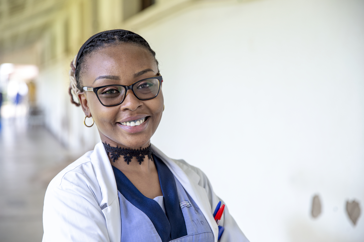 En kvinna med glasögon och labbrock står inomhus med armarna i kors och tittar mot kameran.