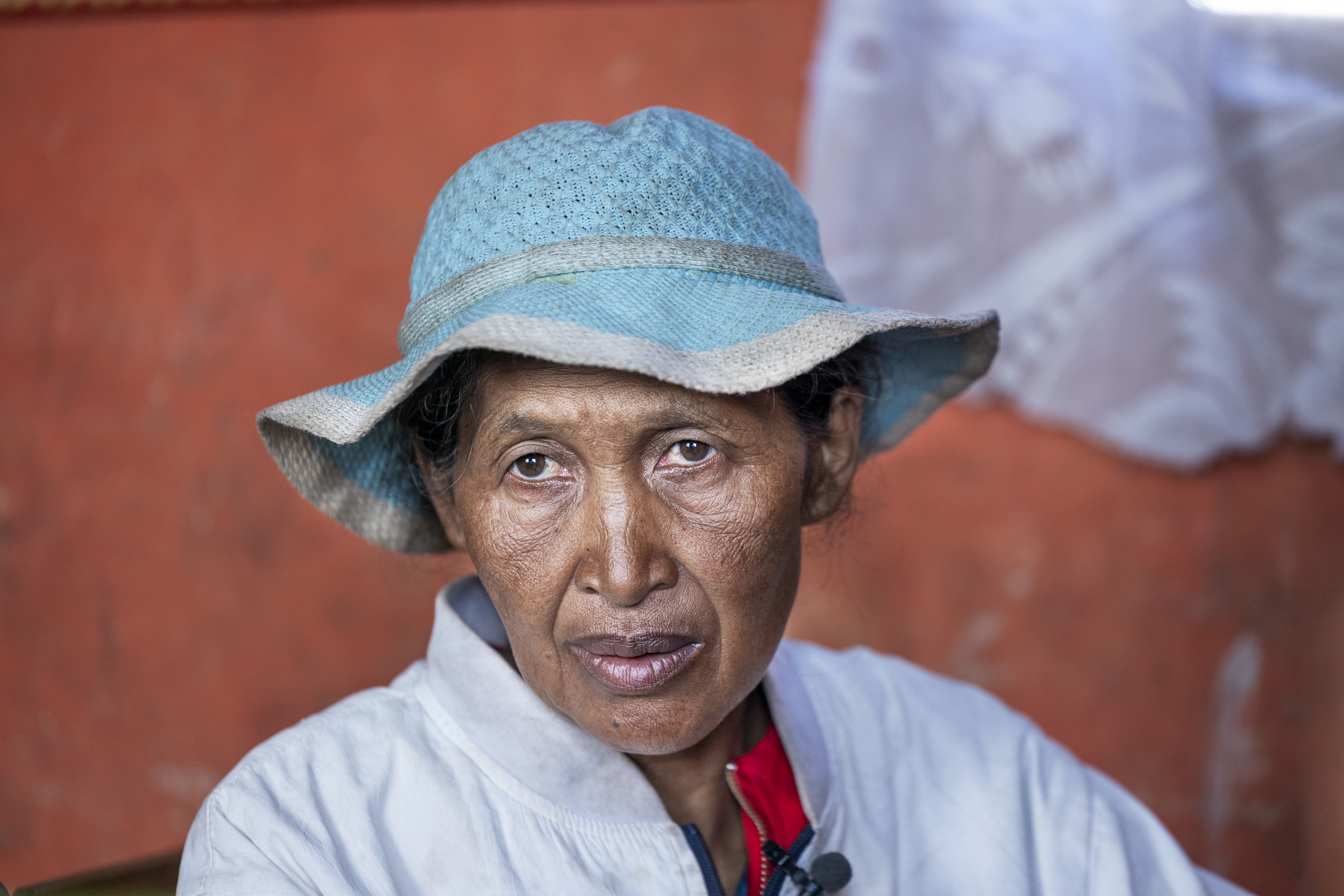 En person med en ljusblå solhatt och en vit jacka tittar mot kameran, mot en orange bakgrund.