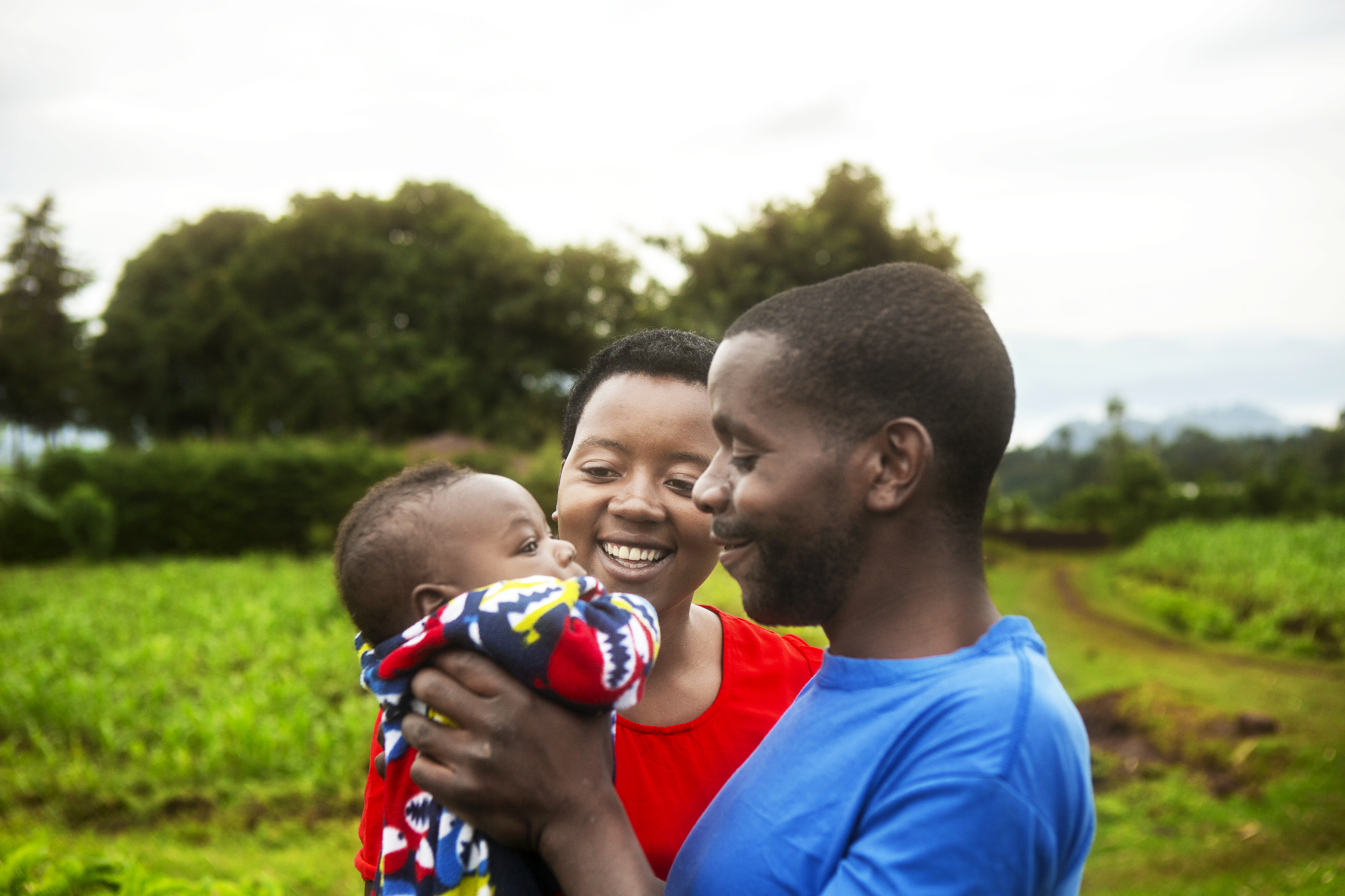En kvinna och man på ett grönt fält håller upp sitt lilla barn och ler.