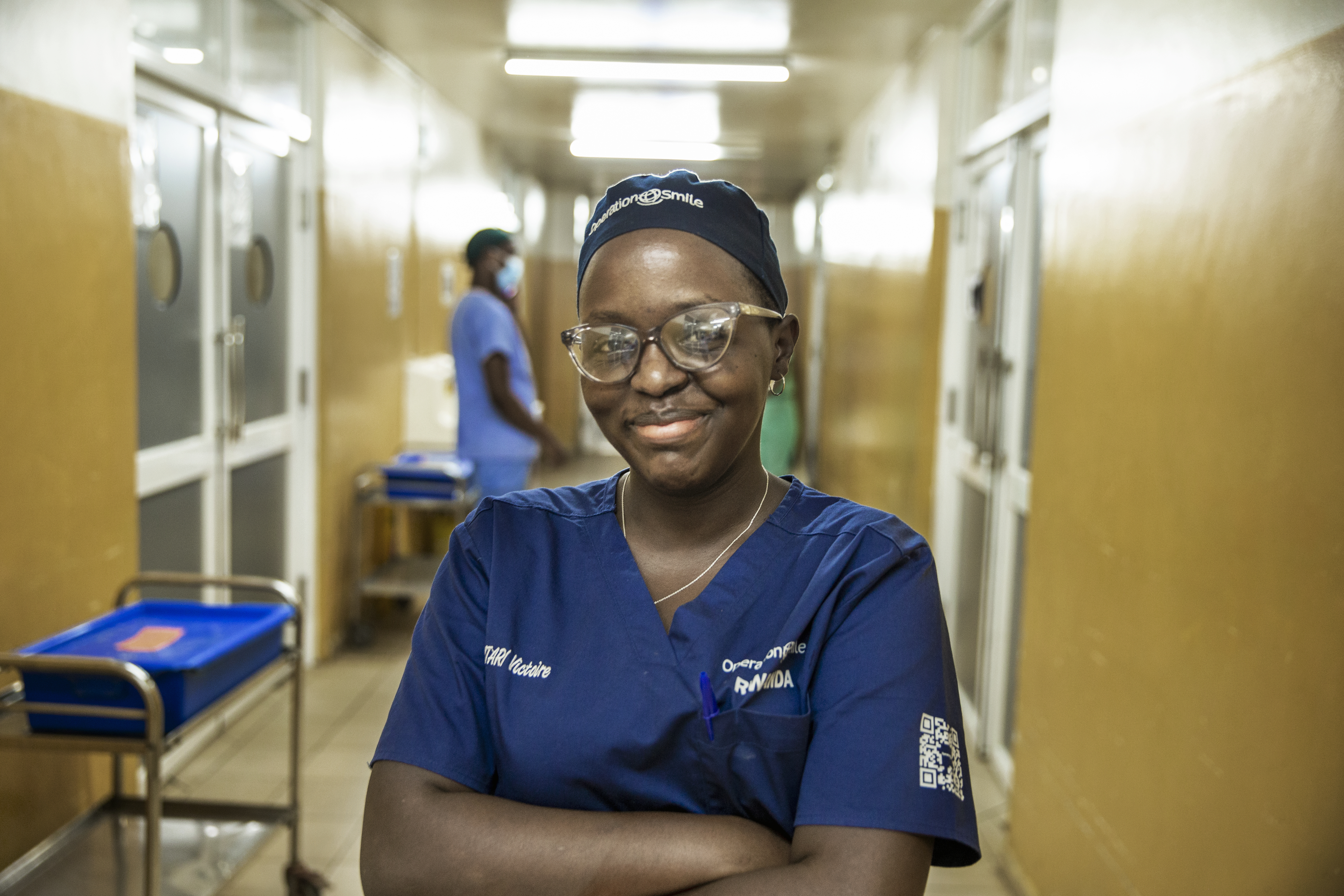 En ung blivande kirurg, Rwandas andra kvinnliga, står i en sjukhuskorridor med armarna i kors. Hon ser glad ut.