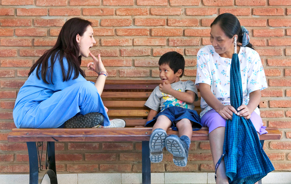 En logoped gör talövningar med en patient på en bänk. Bredvid pojken, patienten, sitter hans mamma.
