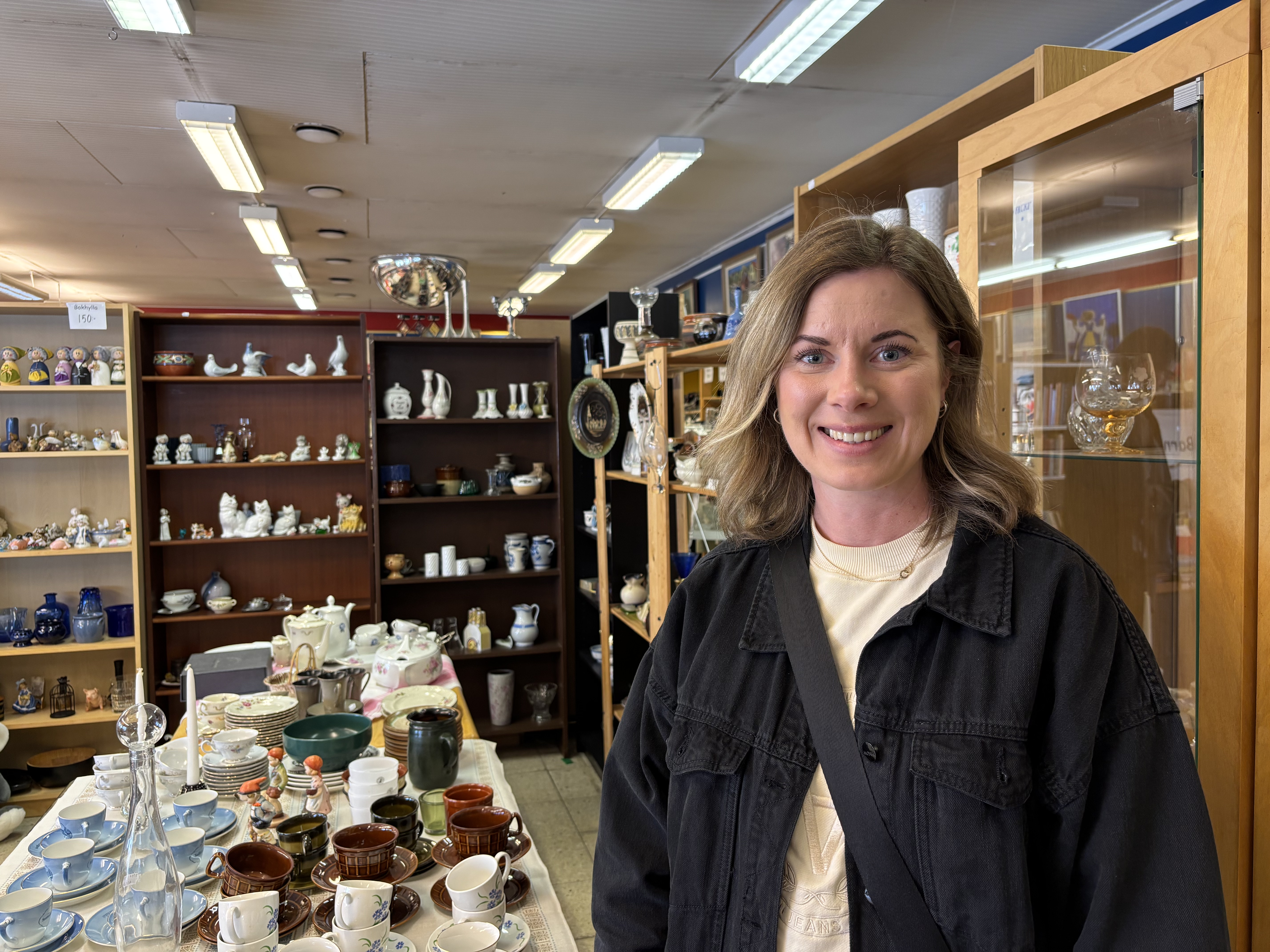 En ung kvinna shoppar inne på Vingåker Second Hand. Hon ser leende in i kameran.