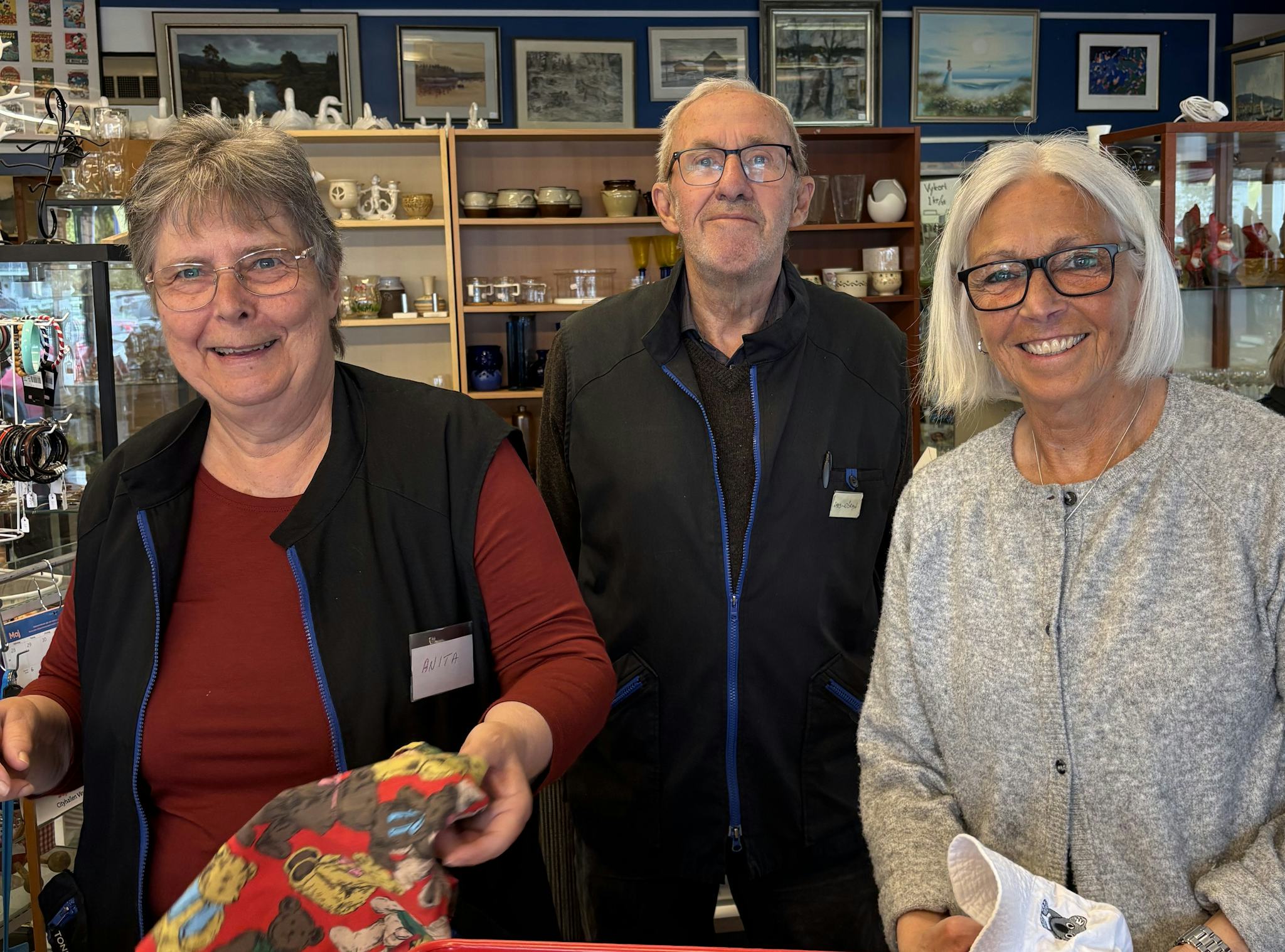 Två kvinnor och en man som arbetar på Vingåker Second Hand ser leende in i kameran.