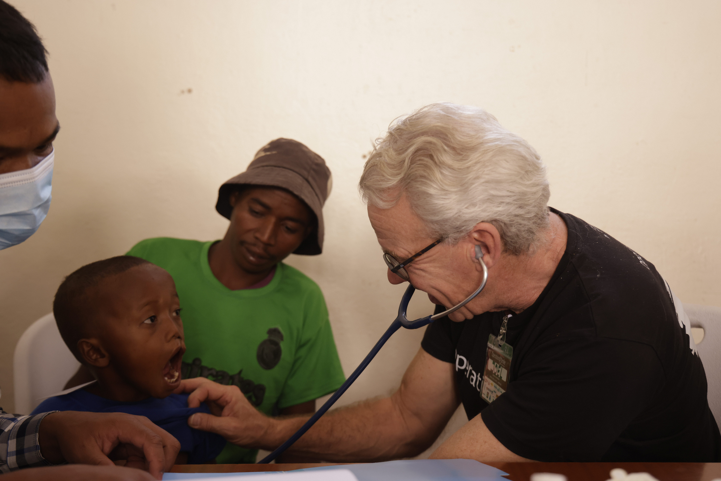 En liten pojke blir undersökt med stetoskop av en läkare, en del av förberedelserna för att bli godkänd för en läpp-käk-gomspalt-operation. Pojkens sitter tryggt i sin pappas knä under tiden han blir undersökt.