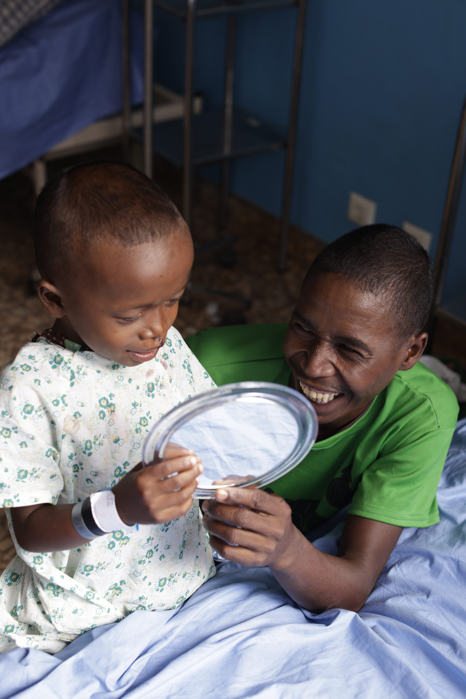 En liten pojke i sjukhuslinne sitter med sin pappa och tittar sig i spegeln efter att han vaknat upp från sin operation. Pojken har opererat sin läppspalt.