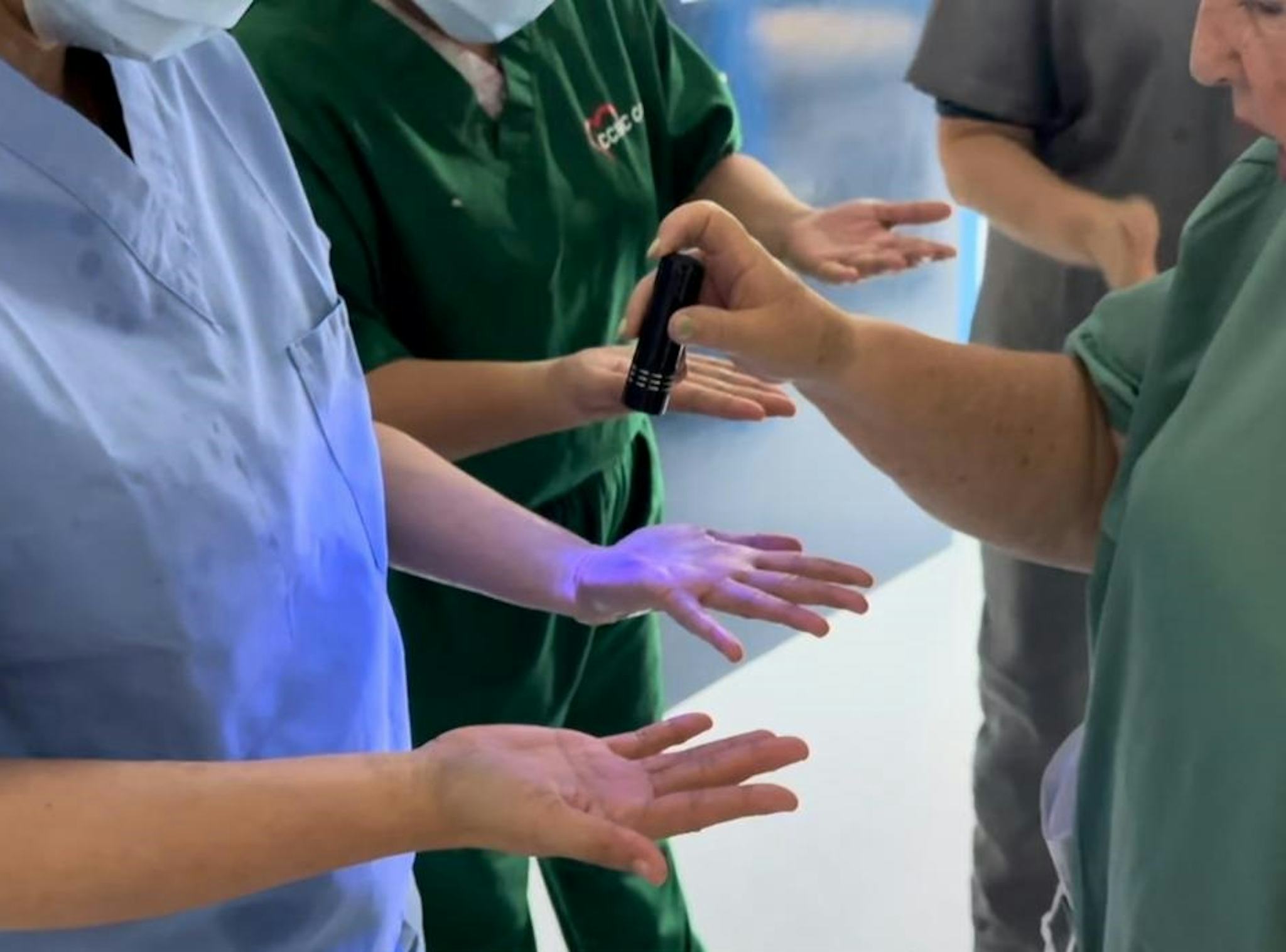 Flera personer i arbetskläder och munskydd granskar sina händer under UV-ljus som visar om det finns ämnen på huden.