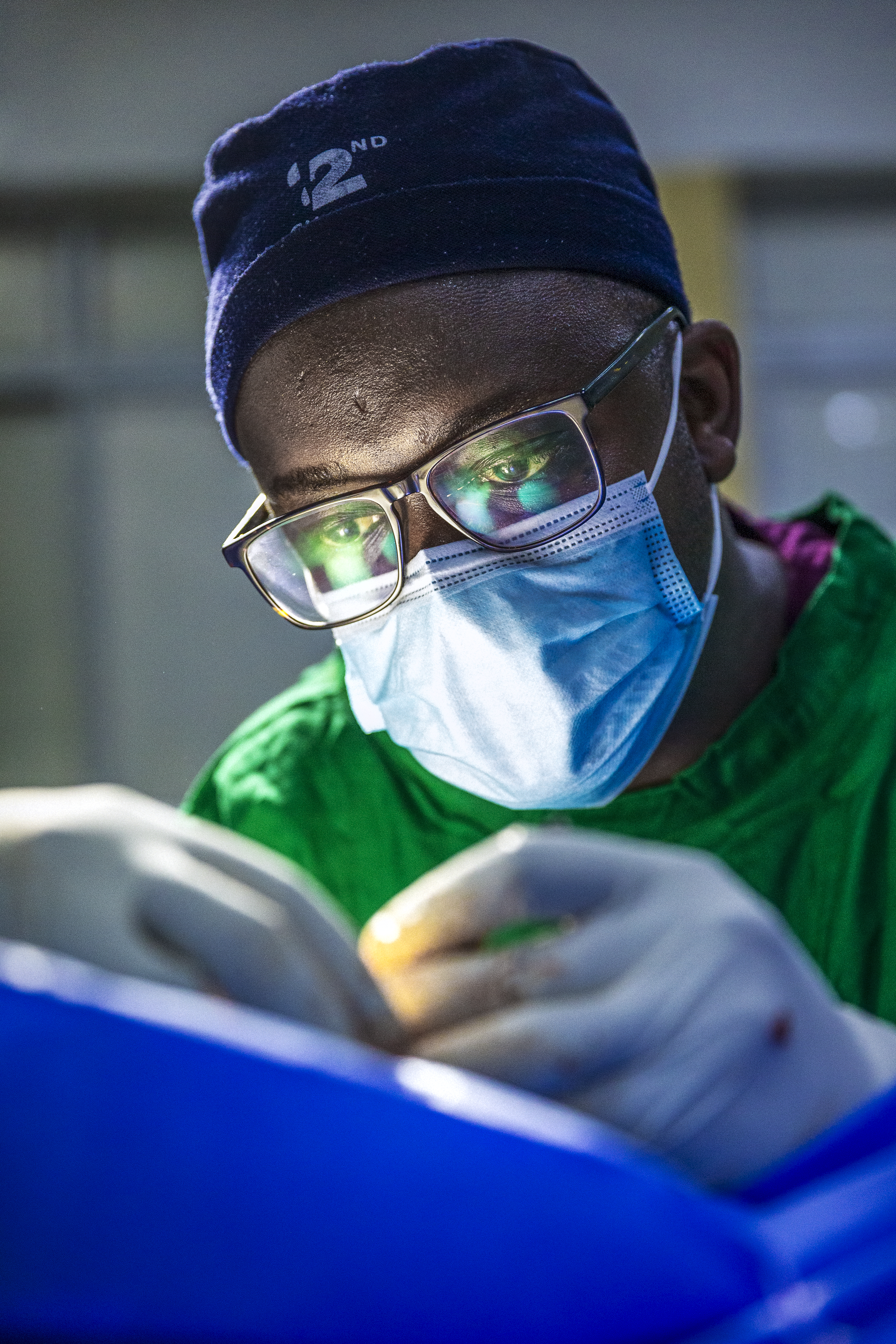 En kirurg med munskydd, glasögon och operationsmössa utför ett ingrepp i en operationssal.