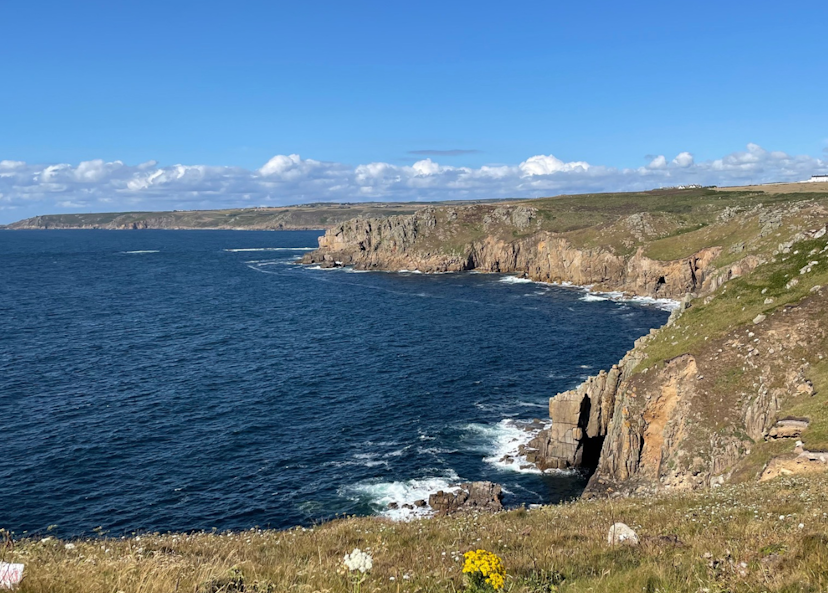 Kustklippor med gräs i förgrunden vid havet under en himmel med några moln.