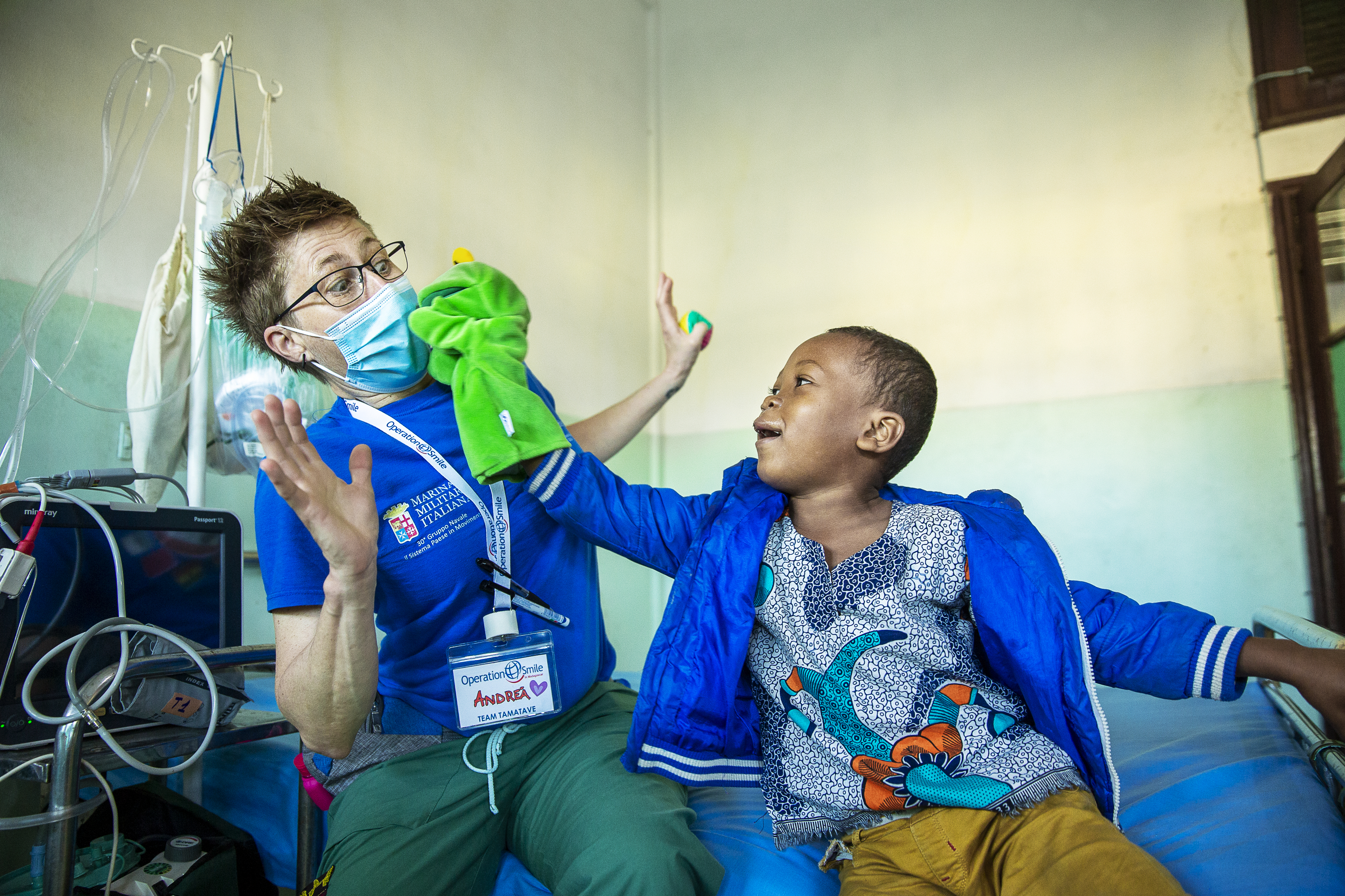 En vårdarbetare interagerar med ett barn som ligger på en sjukhussäng; medicinsk utrustning syns i bakgrunden.