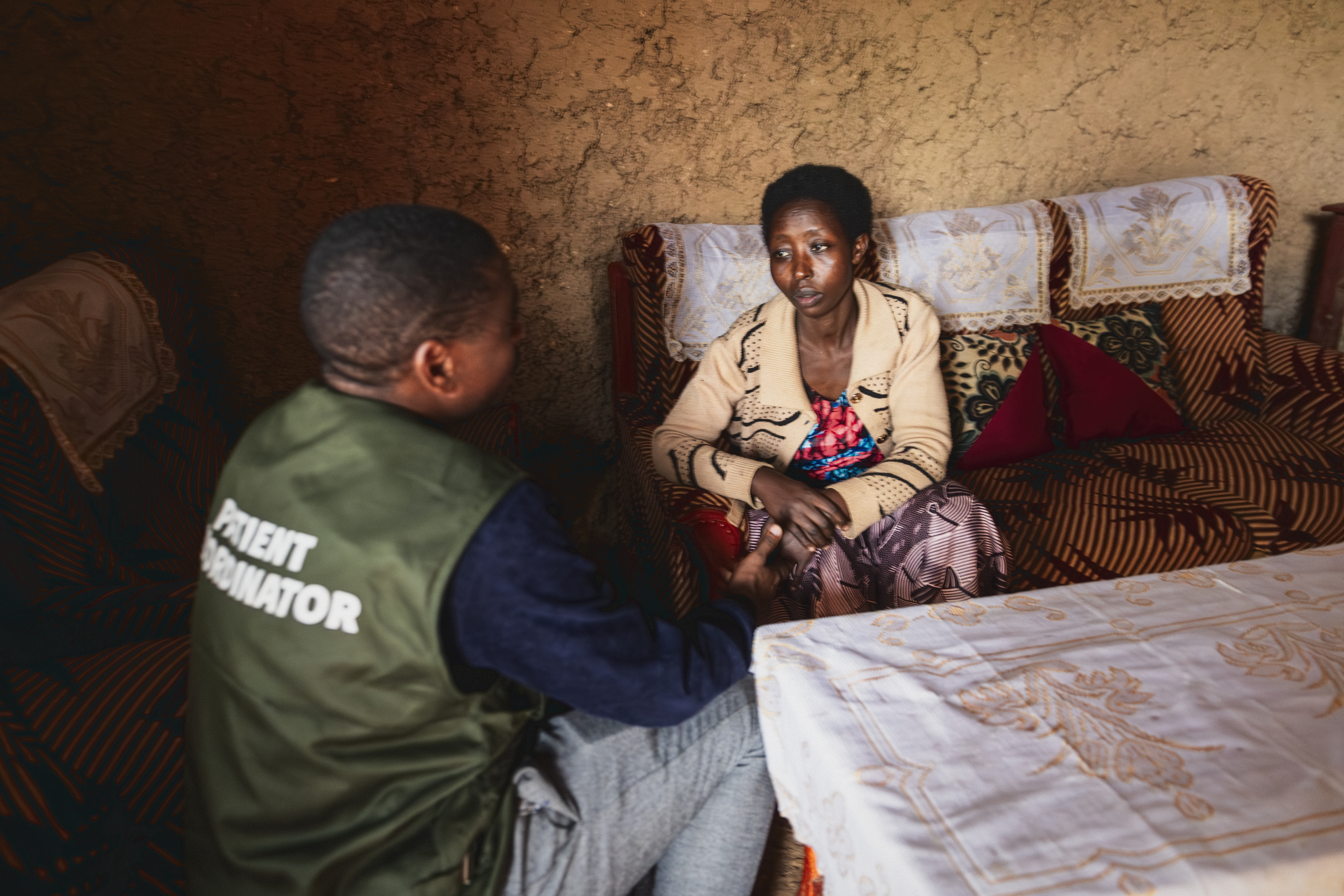 En kvinna sitter på en soffa och pratar med en person som bär en väst märkt PATIENT COORDINATOR i ett rum.