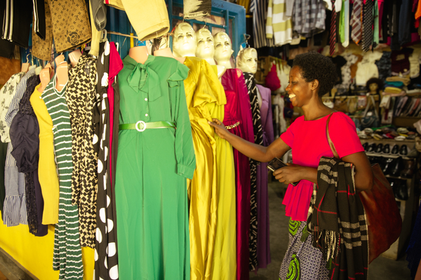 En kvinna ler medan hon tittar på klänningar som sitter på skyltdockor vid ett klädstånd.