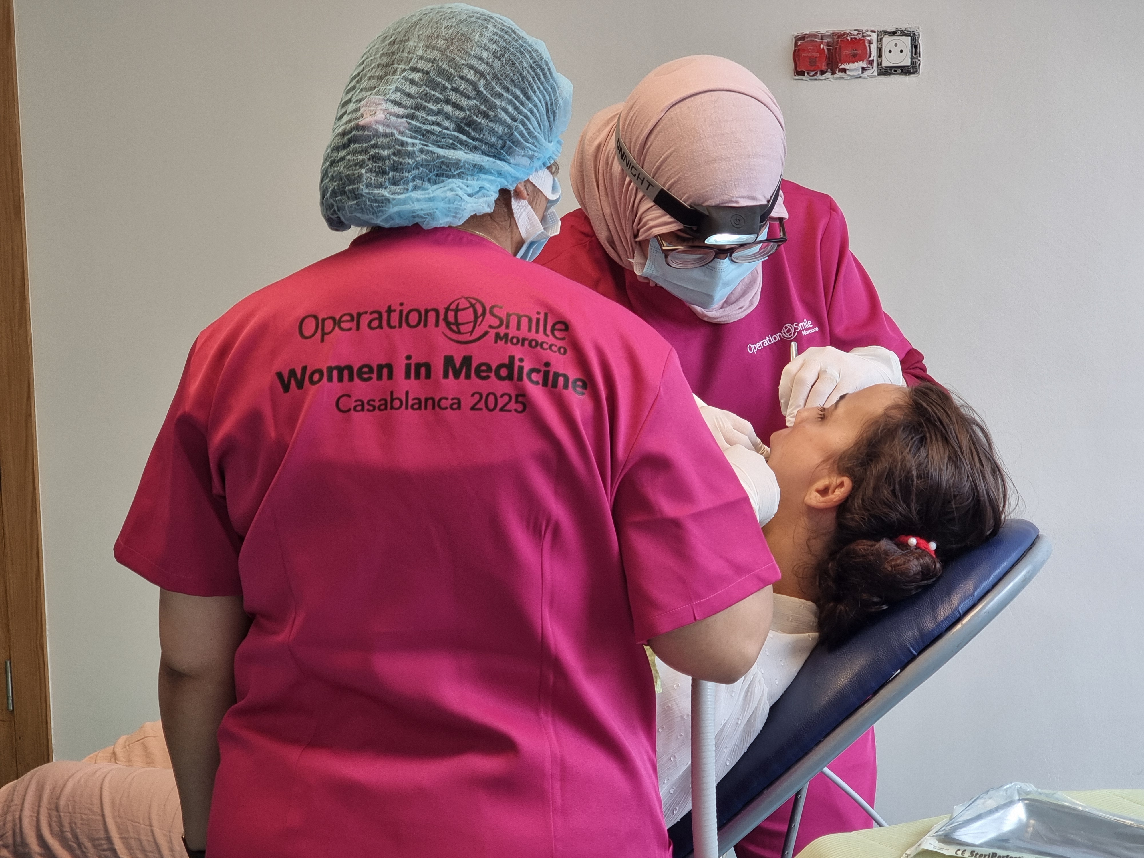 Två kvinnliga medicinska yrkespersoner i rosa uniformer behandlar en patient i en tandläkarstol; på uniformerna står Operation Smile Morocco, Women in Medicine, Casablanca 2025.