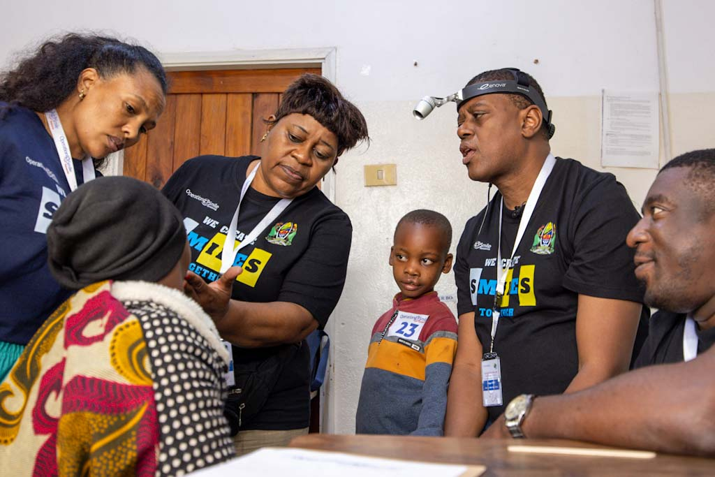 En grupp vårdpersonal och ett barn står runt en sittande patient på en klinik och pratar samt genomför en bedömning.