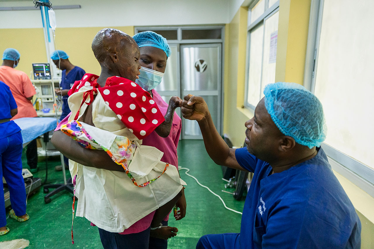 En läkare gör en fistbump med ett barn med brännskador som hålls av en sjuksköterska på sjukhus.